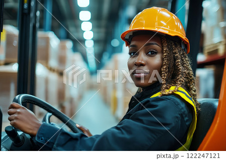 Black woman operates an electric stacker inside an industrial warehouse. Black woman operates an electric stacker inside an industrial warehouse. 122247121