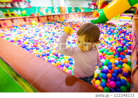 A happy child interacting with colorful balls in a vibrant indoor playground. A happy child interacting with colorful balls in a vibrant indoor playground. 122248115