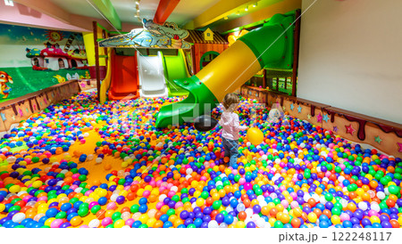 A joyful child with balloons exploring a vibrant ball pit near playground slides. A joyful child with balloons exploring a vibrant ball pit near playground slides. 122248117