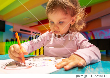 Little girl fully immersed in drawing while enjoying a colorful and creative play environment. Little girl fully immersed in drawing while enjoying a colorful and creative play environment. 122248118
