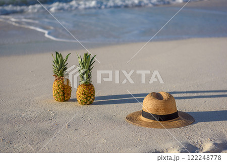 Two pineapples and a hat on white beach sand 122248778
