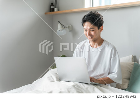 在宅勤務・テレワーク・リモートワーク・在宅ワークで朝ベッドルームでパソコンを使う男性 在宅勤務・テレワーク・リモートワーク・在宅ワークで朝ベッドルームでパソコンを使う男性 122248942