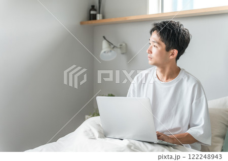 在宅勤務・テレワーク・リモートワーク・在宅ワークで朝ベッドルームでパソコンを使う男性 在宅勤務・テレワーク・リモートワーク・在宅ワークで朝ベッドルームでパソコンを使う男性 122248943