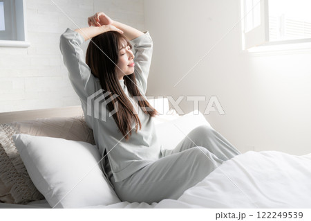 ベッドの上で寝起きで伸びやストレッチをする女性 122249539