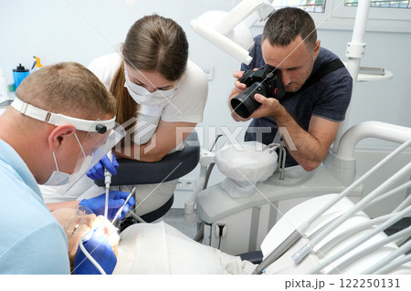 photographer takes pictures of dental treatment process videographer shoots video man Dental treatment. Woman on dental examination. Professional equipment in dental clinic photographer takes pictures of dental treatment process videographer shoots video man Dental treatment. Woman on dental examination. Professional equipment in dental clinic 122250131