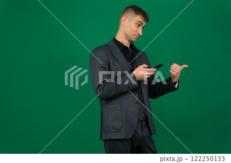emotions of a handsome man guy on a green background chromakey close-up dark hair young man. phone in hand talk dial SMS online call gadget boss work advertising 122250133