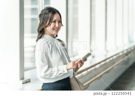 駅のロビーでスマホを使う笑顔の女性（アプリ・モバイルチケット・チケットレス・電子乗車券） 122250541
