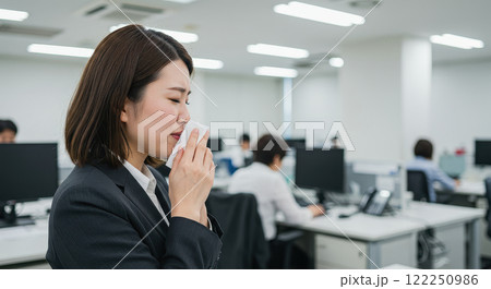 オフィスで寒そうにクシャミをしている女性 122250986