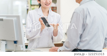 薬局で高齢者・中高年男性にスマホアプリを説明する薬剤師・調剤師の女性(服薬指導) 薬局で高齢者・中高年男性にスマホアプリを説明する薬剤師・調剤師の女性(服薬指導) 122251313