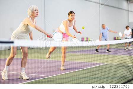 Senior woman playing doubles pickleball with young female partner Senior woman playing doubles pickleball with young female partner 122251793