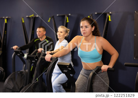 Group of people engaged in a spin bike simulator in the gym, exercising on stationary bike 122251829