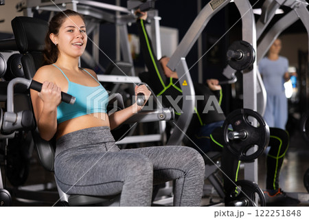 Smiling girl doing bicep curls on gym machine Smiling girl doing bicep curls on gym machine 122251848