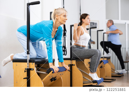 Mature European woman making Pilates exercising while standing on knees using Wanda chair machine at gym 122251881