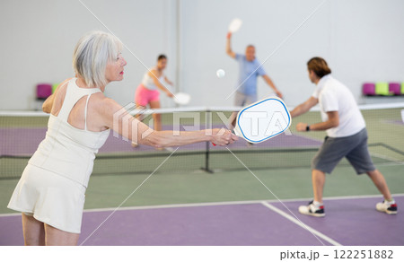 Rear view of aged woman playing pickleball on indoor court 122251882