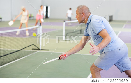 Aged man playing friendly pickleball match on indoor court Aged man playing friendly pickleball match on indoor court 122251989