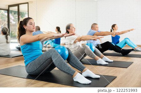 Group of young elderly people in sportswear exercising Pilates with mini balls while lying on mats in rehabilitation center 122251993