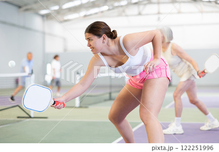 Expressive young girl playing pickleball in indoor court 122251996