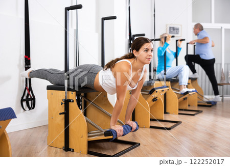 Young European woman training lower back on Pilates Wanda chair machine during her health exercise at studio 122252017