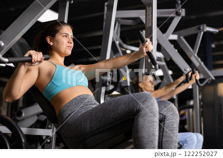 Fit young woman working out at chest press machine 122252027
