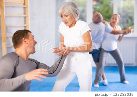 Senior woman in pair with middle-aged coach train Krav Maga and self-defense skills. 122252039