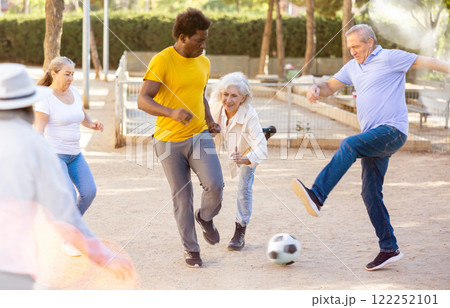 Excited elderly multiracial people playing street football on the playground on a sunny weather Excited elderly multiracial people playing street football on the playground on a sunny weather 122252101