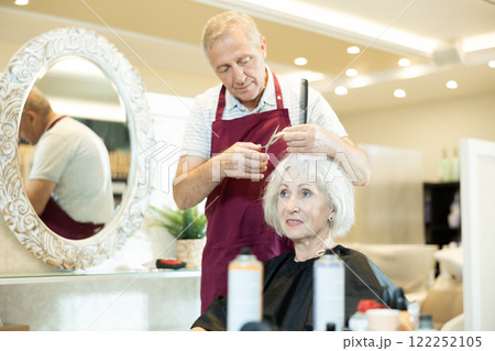 Experienced senior man master makes performs haircut for mature woman with scissors Experienced senior man master makes performs haircut for mature woman with scissors 122252105