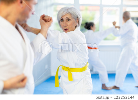 Group of mature people in kimono sparring together in gym during karate training Group of mature people in kimono sparring together in gym during karate training 122252144