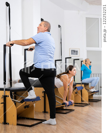 Mature man performing standing Pilates exercise on Wanda chair in fitness studio Mature man performing standing Pilates exercise on Wanda chair in fitness studio 122252251
