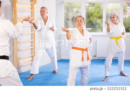 Old woman attendee of karate classes practicing kata standing in row with others 122252322