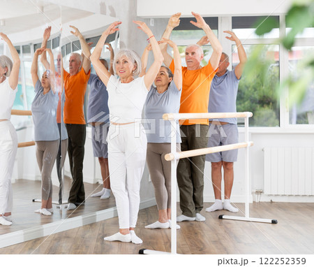 Active mature woman practicing fifth position holding by ballet barre together with others Active mature woman practicing fifth position holding by ballet barre together with others 122252359