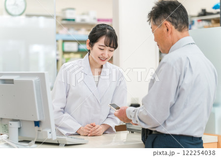 薬局で高齢者・中高年男性にスマホアプリを説明する薬剤師・調剤師の女性(服薬指導) 薬局で高齢者・中高年男性にスマホアプリを説明する薬剤師・調剤師の女性(服薬指導) 122254038