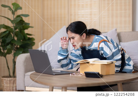 A young Asian entrepreneur feels stressed while selling online through online platforms because she has trouble organizing orders and packing products into boxes for delivery. 122254208