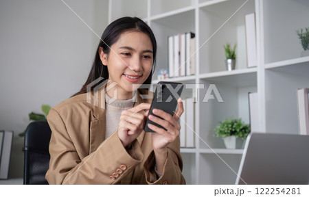 Young Asian business woman sits on the phone in an online business meeting using a laptop in a modern home office decorated with shady green plants. 122254281