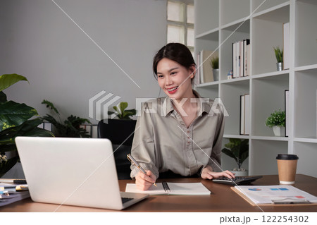 Young Asian business woman sitting in the office using a calculator to calculate business numbers. Young Asian business woman sitting in the office using a calculator to calculate business numbers. 122254302