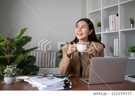 Young Asian business woman sits and works using a laptop in a modern office decorated with shady green plants. 122254317