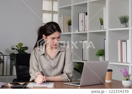 Young Asian business woman sitting in the office using a calculator to calculate business numbers. Young Asian business woman sitting in the office using a calculator to calculate business numbers. 122254370
