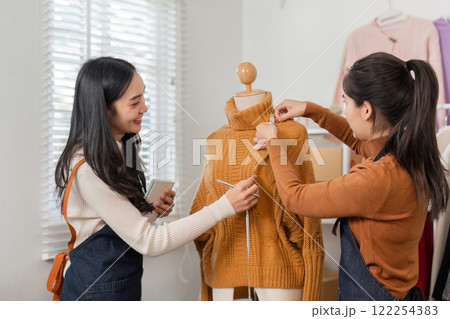 Fashion designers collaborating and measuring a knitted sweater on a mannequin, highlighting teamwork in a vibrant boutique Fashion designers collaborating and measuring a knitted sweater on a mannequin, highlighting teamwork in a vibrant boutique 122254383