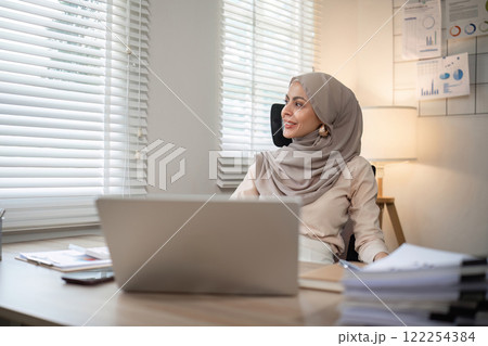 Muslim female entrepreneur wearing hijab sits working with laptop managing personal business in private office. 122254384