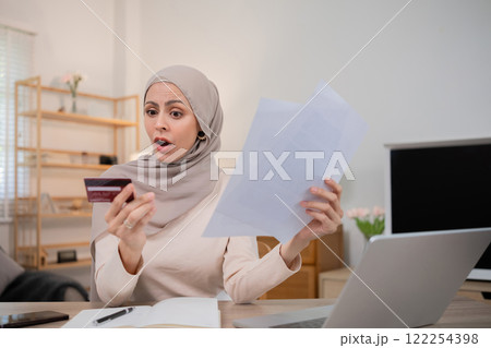A young Muslim woman is shocked by an excessive bill from an online purchase made with a credit card through an online banking application. A young Muslim woman is shocked by an excessive bill from an online purchase made with a credit card through an online banking application. 122254398