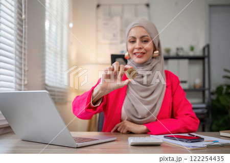 A female Muslim investor who trades in cryptocurrencies sits looking at stock charts and studying Bitcoin. A female Muslim investor who trades in cryptocurrencies sits looking at stock charts and studying Bitcoin. 122254435