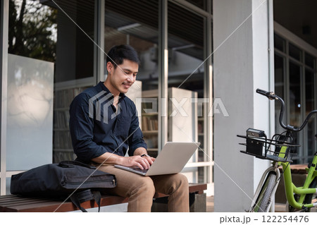 A young Asian businessman rides a bicycle to work. Use a reusable water bottle. Working outside of the office using a laptop The concept of saving energy and reducing pollution to the environment. A young Asian businessman rides a bicycle to work. Use a reusable water bottle. Working outside of the office using a laptop The concept of saving energy and reducing pollution to the environment. 122254476