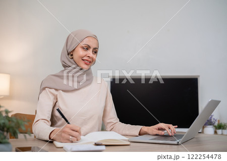 A young Muslim woman wearing a hijab calculates financial accounts. Income and expenses in the living room at home 122254478