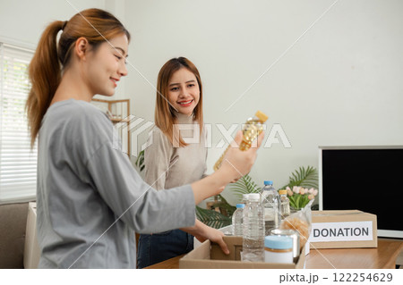 Two young female volunteers help pack food into donation boxes and prepare to donate them to charity. Two young female volunteers help pack food into donation boxes and prepare to donate them to charity. 122254629
