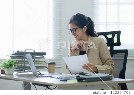 Asian businesswoman or accountant happily sitting and working with laptop on finance and business administration. On the desk in the office decorated with green plants. 122254702