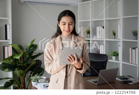 Asian businesswoman holding online business meeting via tablet in modern home office decorated with lush green plants. 122254708