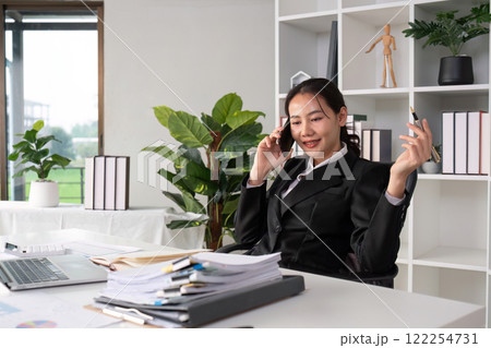 Asian female accountant Discussing business over the phone in an office with work plan documents on the table 122254731