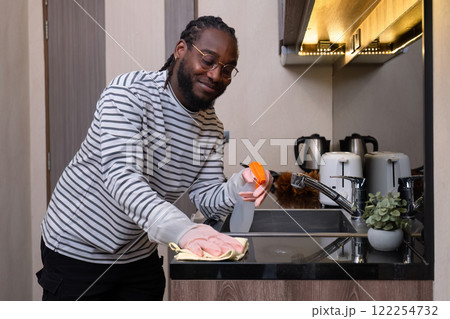 Happy young African American man dressed at home, doing housework, mopping the floor, cleaning the room on his day off. 122254732