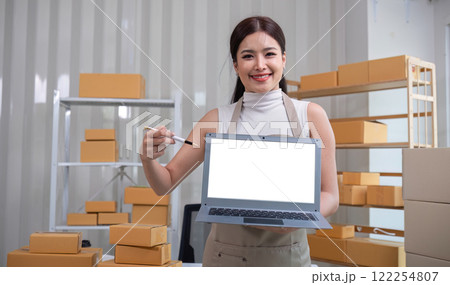 A small SME business owner stands holding a laptop with a white screen. Use a laptop to record small business information in your home office. A small SME business owner stands holding a laptop with a white screen. Use a laptop to record small business information in your home office. 122254807