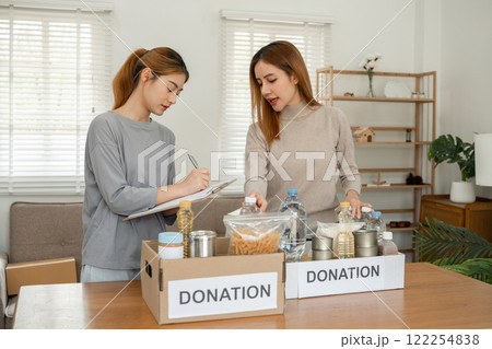 Two young female volunteers help pack food into donation boxes and prepare to donate them to charity 122254838