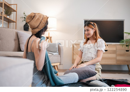 Two young female friends have fun packing supplies and clothes and discussing plans for a vacation together. 122254890